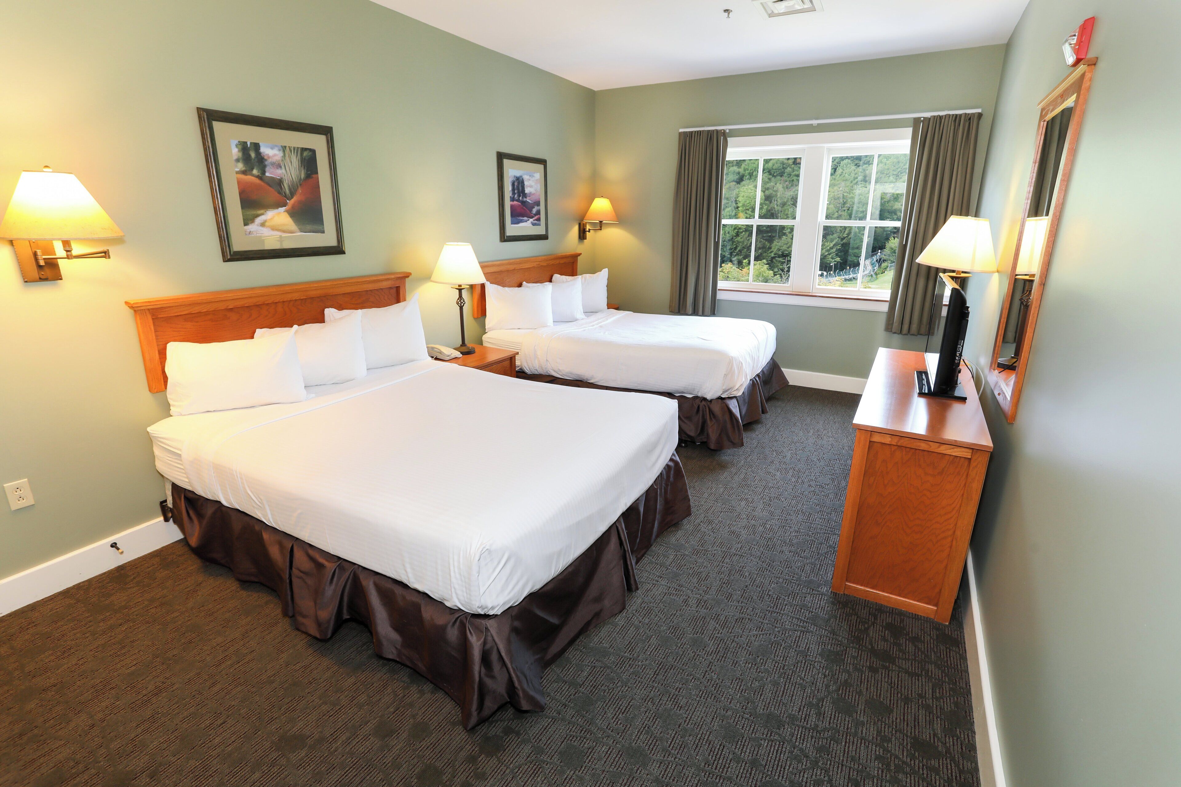 A hotel room with two beds, a window with curtains, and two wall-mounted lamps.