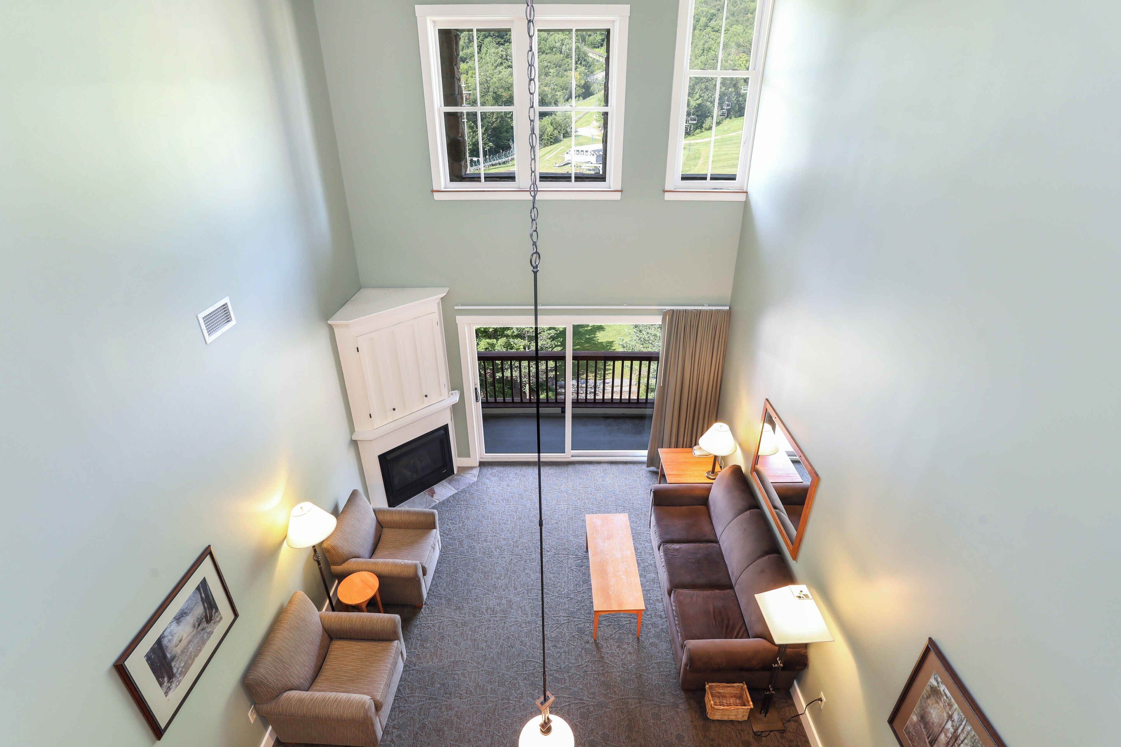 A high-ceilinged living room with a fireplace, two sofas, a coffee table, and a hanging light fixture.