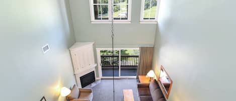 A high-ceilinged living room with a fireplace, two sofas, a coffee table, and a hanging light fixture.