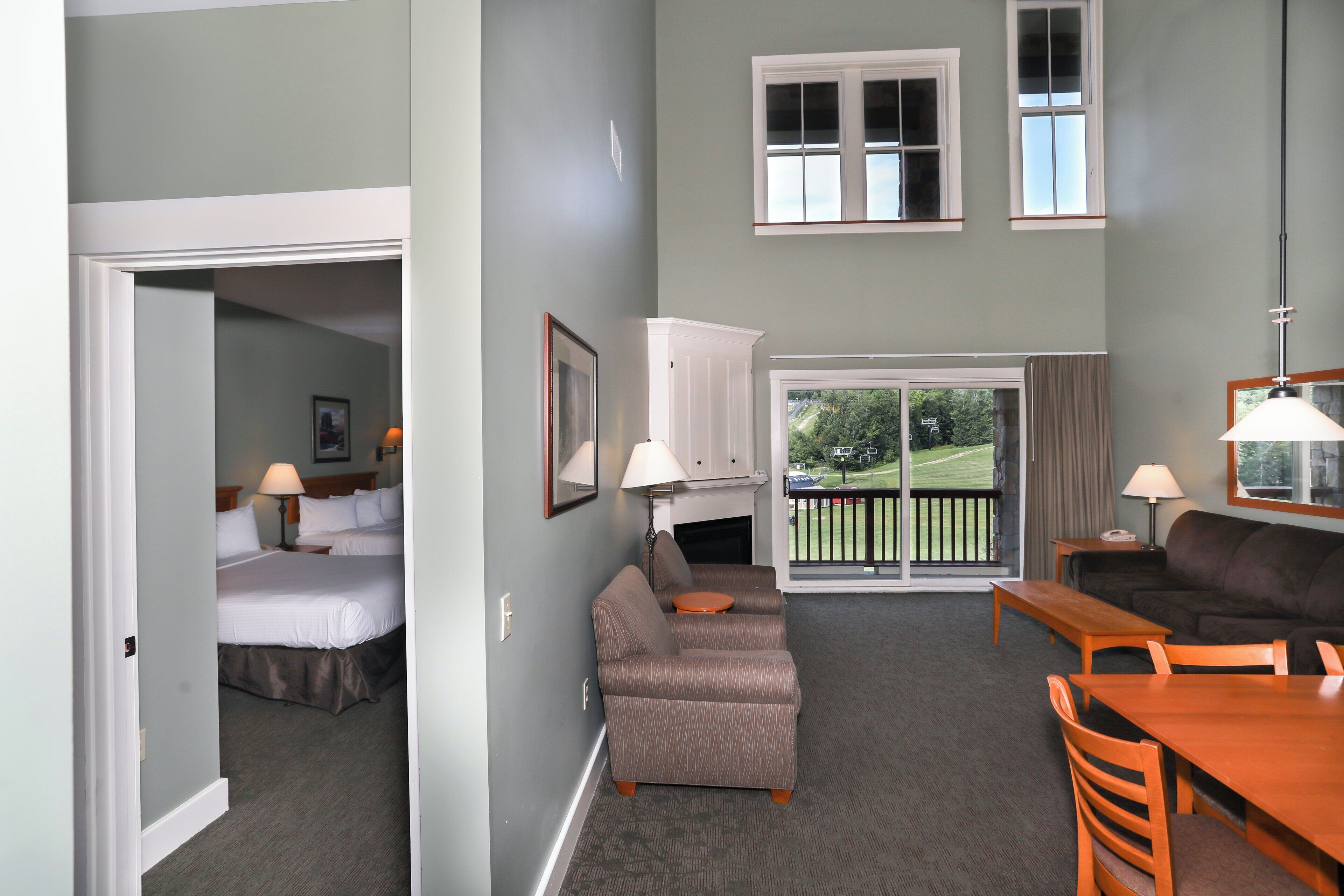 A hotel room with a bed, a sofa, a dining table, and a balcony with a view of the outdoors.