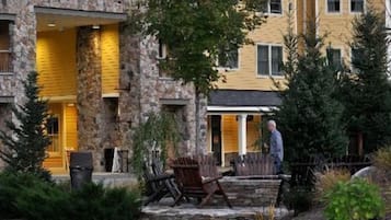Un edificio de piedra con fachada amarilla, mesas al aire libre y una persona caminando.
