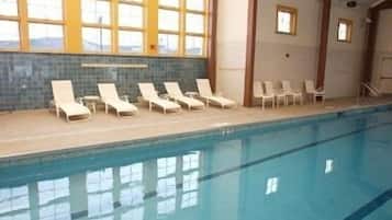 Une piscine intérieure dotée de chaises longues et offrant une vue sur les montagnes grâce à de grandes fenêtres.