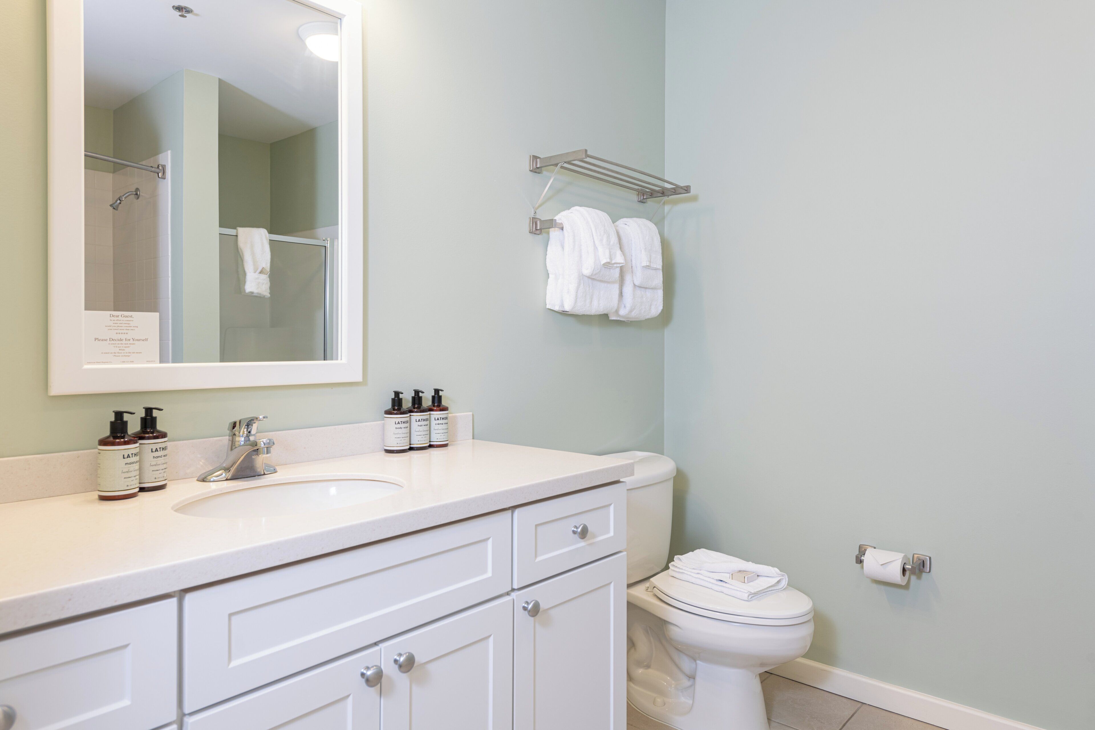A bathroom with a white sink, mirror, and toilet. There are two bottles of lotion on the sink.
