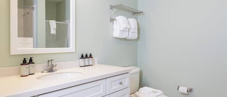 A bathroom with a white sink, mirror, and toilet. There are two bottles of lotion on the sink.