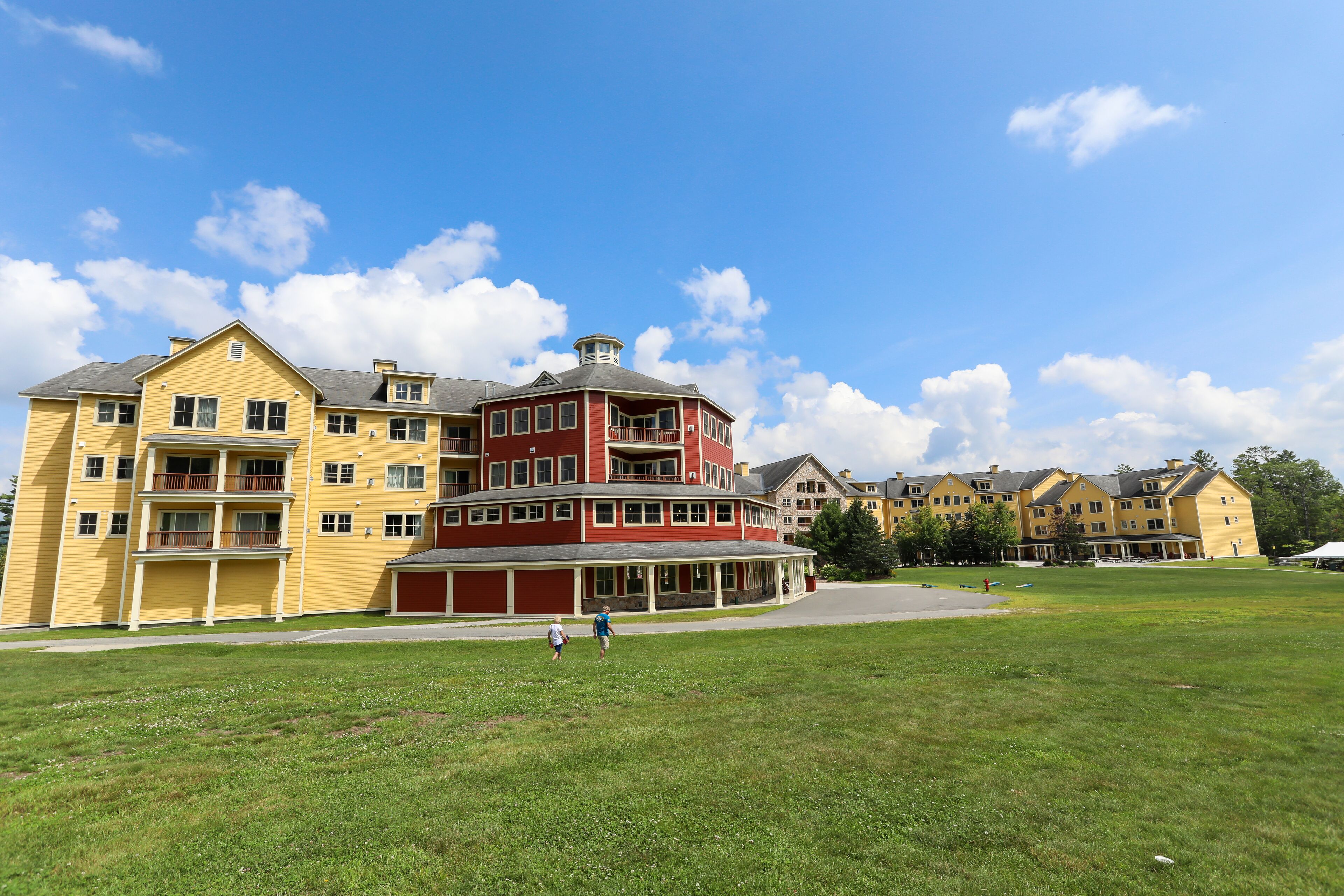 A multi-story building with a central red tower, surrounded by a grassy area and other buildings.
