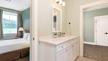 A hotel room with a bed, a bathroom with a sink and mirror, and a view of a green landscape through the window.