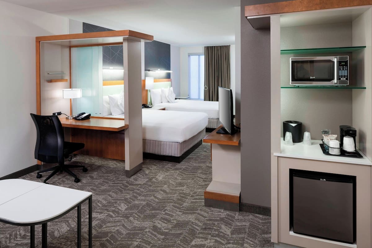 Quarto de hotel com escrivaninha, duas camas, televisão, micro-ondas e mini-geladeira.