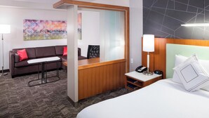Una habitación de hotel con cama, escritorio, sofá, espejo y un cuadro en la pared.