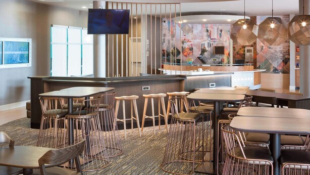 Un restaurante moderno con zona de bar, diversas opciones de asientos y una gran pantalla de televisión.