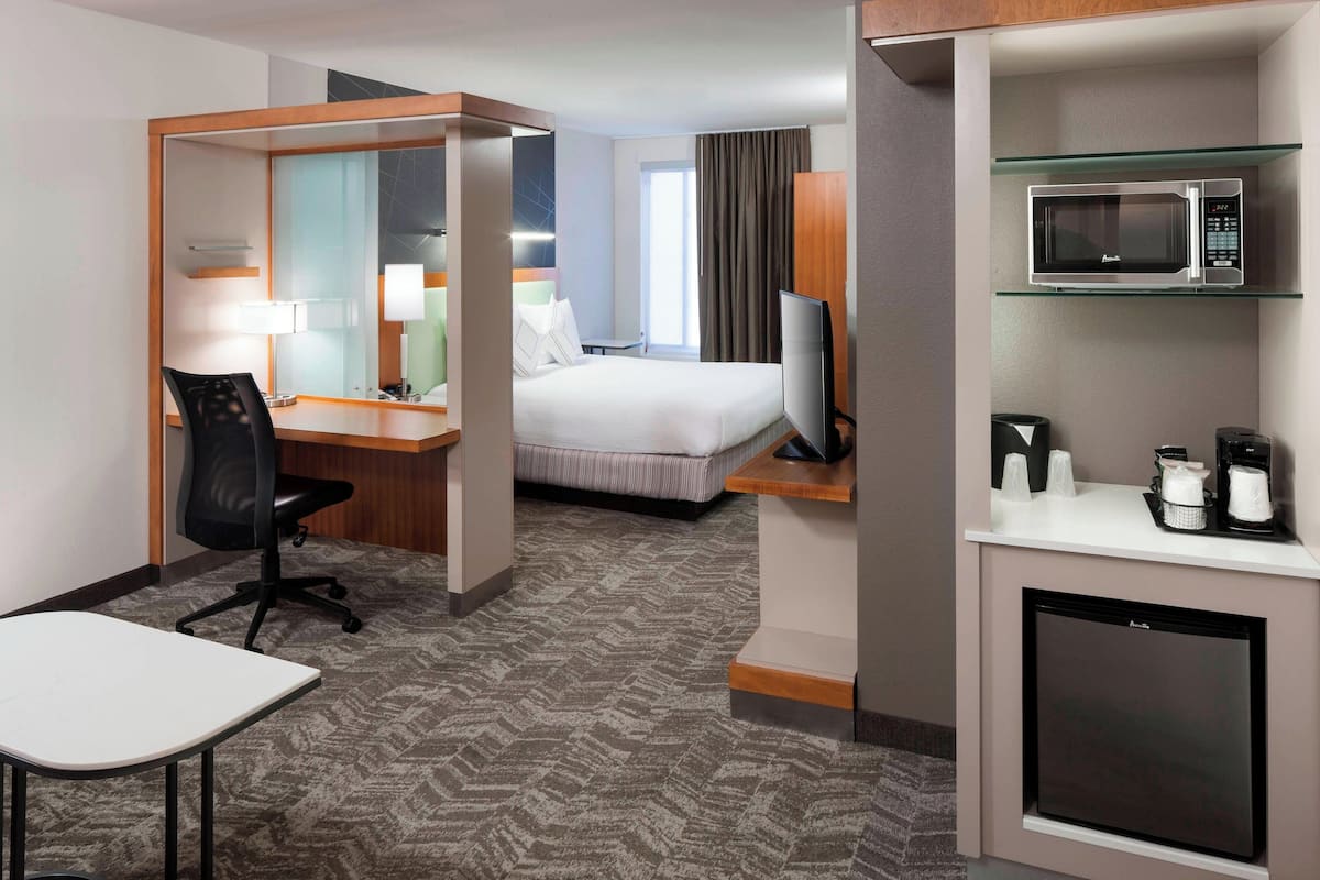 Quarto de hotel com cama, escrivaninha, cadeira, televisão, micro-ondas e mini-geladeira.
