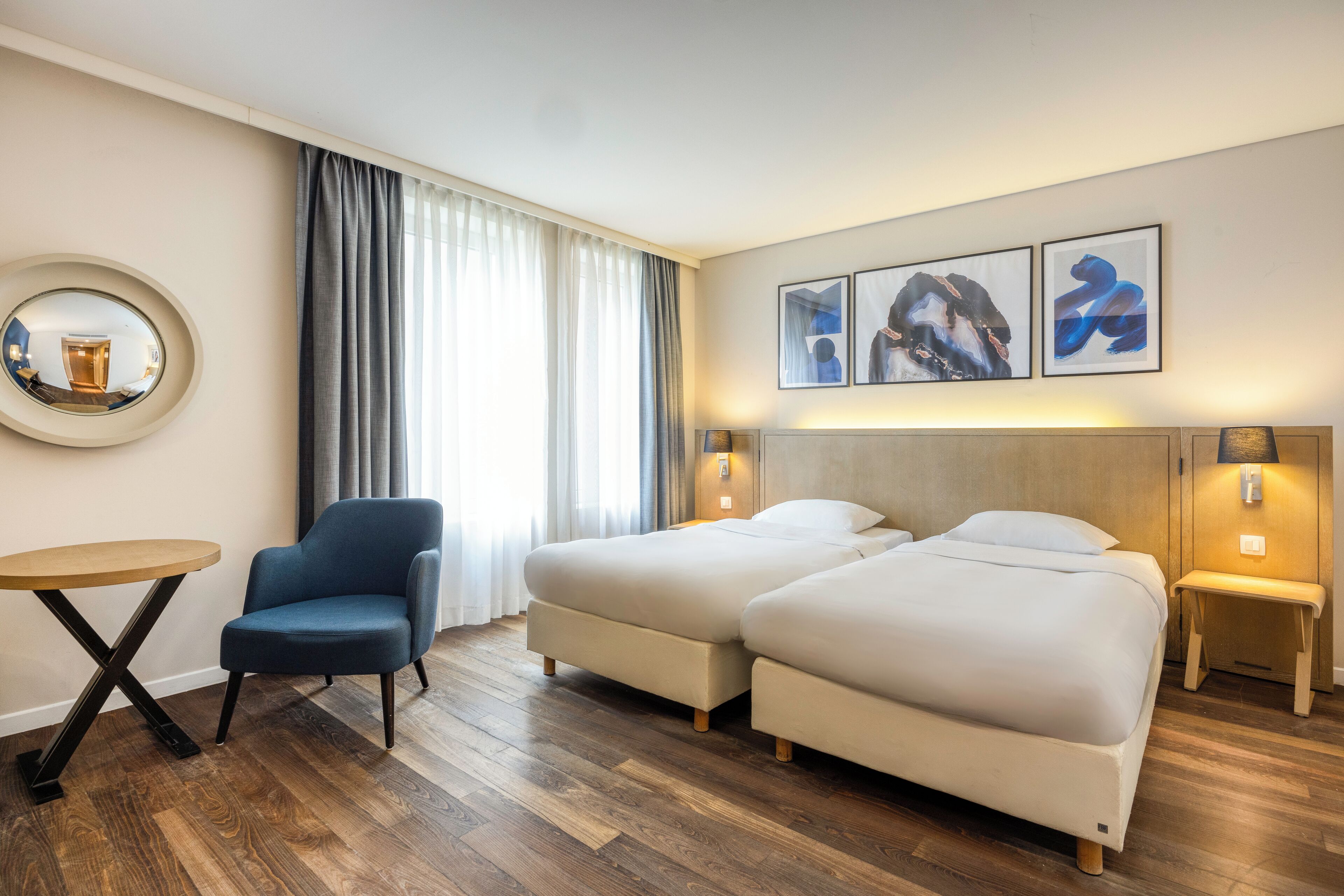 Une chambre d’hôtel avec deux lits, une table ronde, une chaise et des œuvres d’art accrochées au mur.