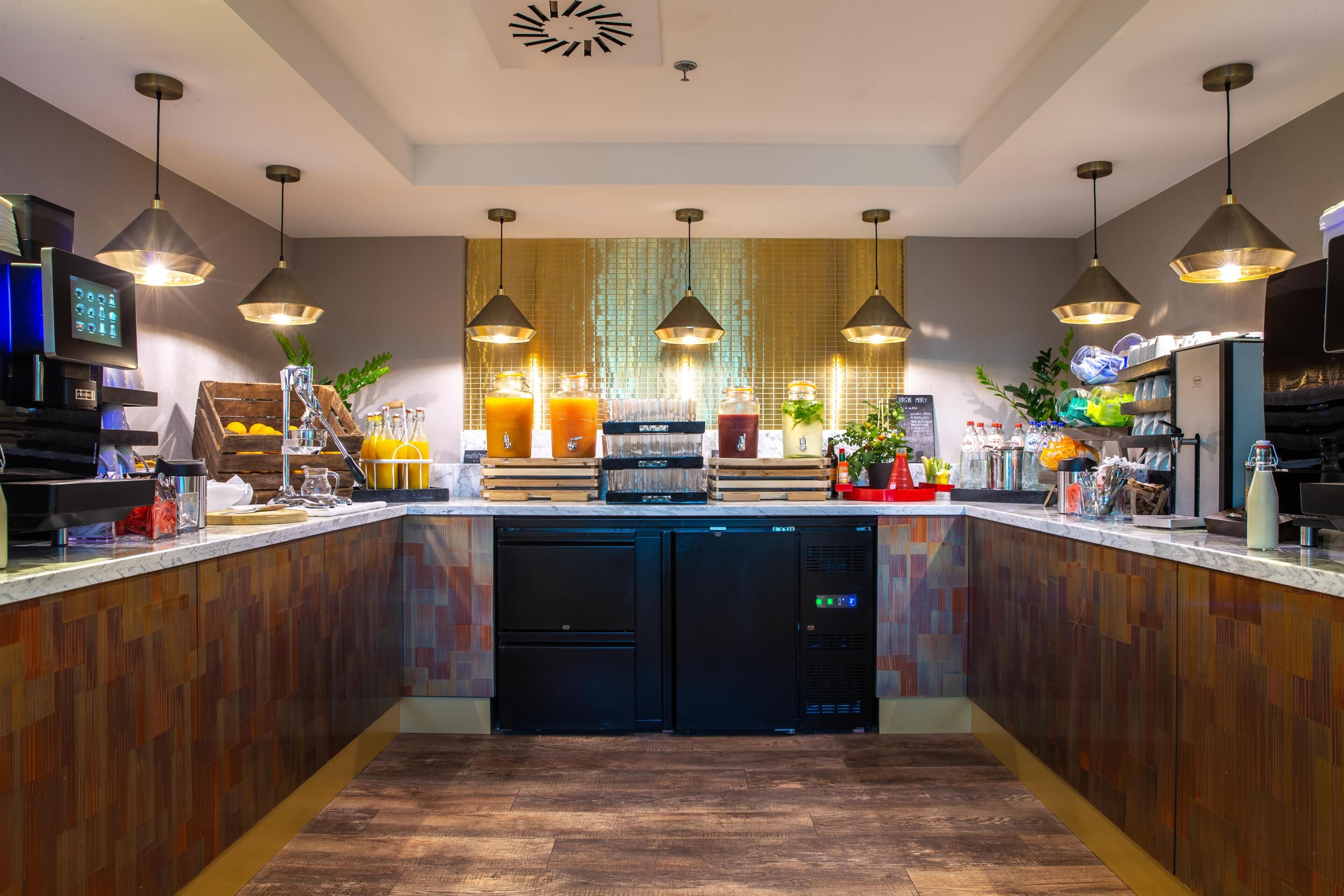 Une cuisine moderne avec des meubles en bois, des appareils électroménagers intégrés, des luminaires suspendus et un îlot central doté d’un réfrigérateur.