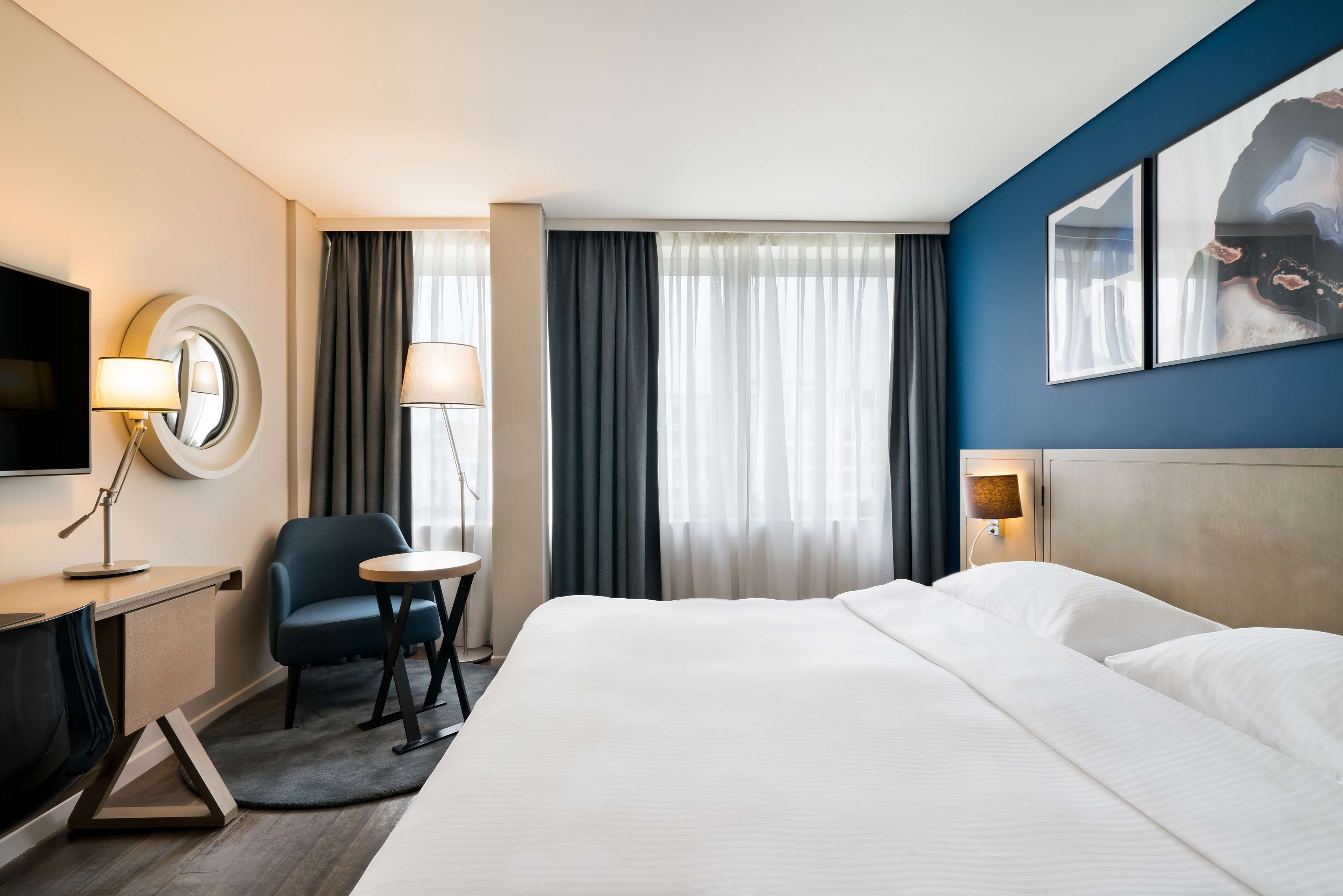Une chambre d’hôtel équipée d’un lit, d’un bureau, d’une chaise, d’une télévision et d’une fenêtre avec des rideaux.