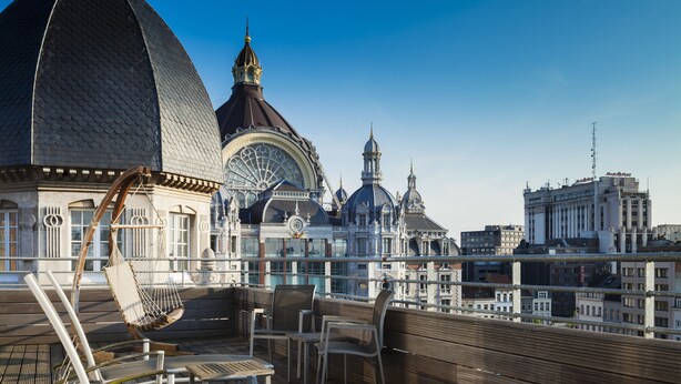 Une terrasse sur le toit, dotée de chaises longues et d’un hamac, offrant une vue sur le paysage urbain, avec ses bâtiments historiques et ses dômes.