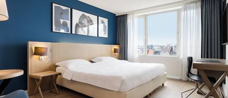 Habitación de hotel con una cama grande, un escritorio y vistas a la ciudad.