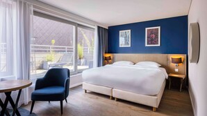 Une chambre d’hôtel avec un grand lit, deux lampes de chevet, une chaise, une petite table et une vue sur l’extérieur.