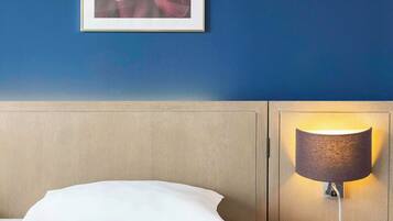 A hotel room with a bed, a wall-mounted lamp, and a framed floral artwork.