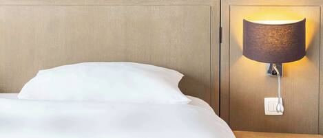 A hotel room with a bed, a wall-mounted lamp, and a framed floral artwork.