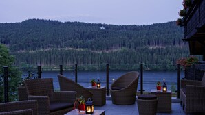 Wicker furniture arranged on a terrace with a view of a lake and forest. - Boutique-Hotel Alemannenhof (Hinterzarten)