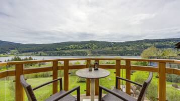 A balcony with wicker chairs and a table, overlooking a lake and forested hills.