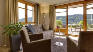 A living room with a sofa, chairs, a potted plant, and a view of a deck with outdoor furniture. - Boutique-Hotel Alemannenhof (Hinterzarten)
