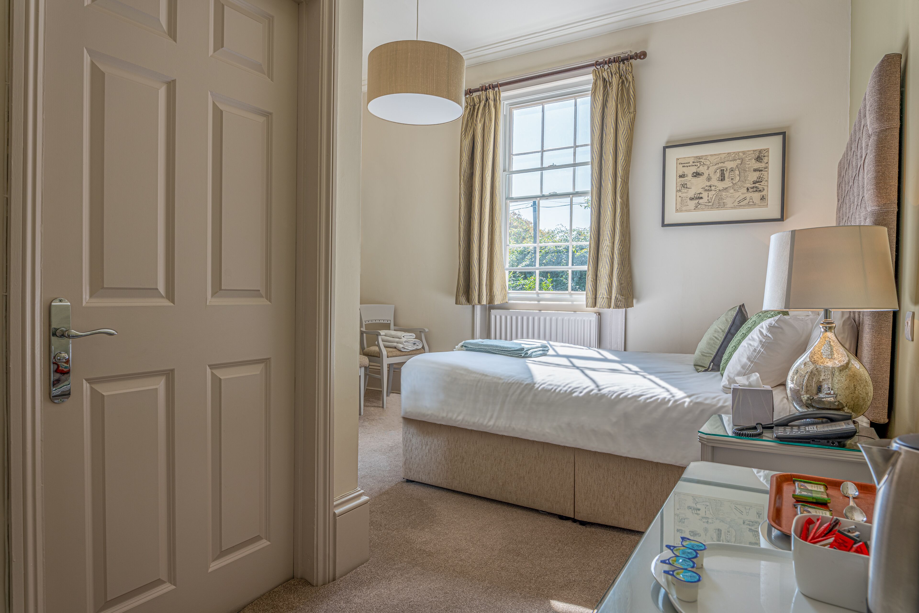 A hotel room with a bed, bedside table, lamp, and a window with curtains.