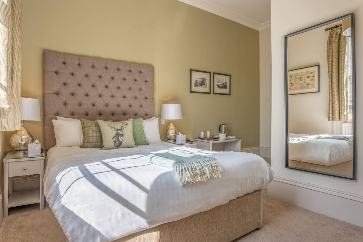A neatly arranged bedroom with a large bed, two bedside tables, a nightstand, and a mirror on the wall.