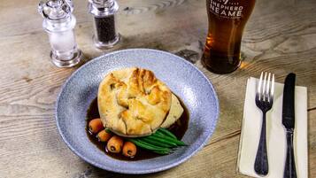 A plate of food with a pastry, green beans, and carrots, accompanied by a glass of beer and salt and pepper shakers on a wooden table.