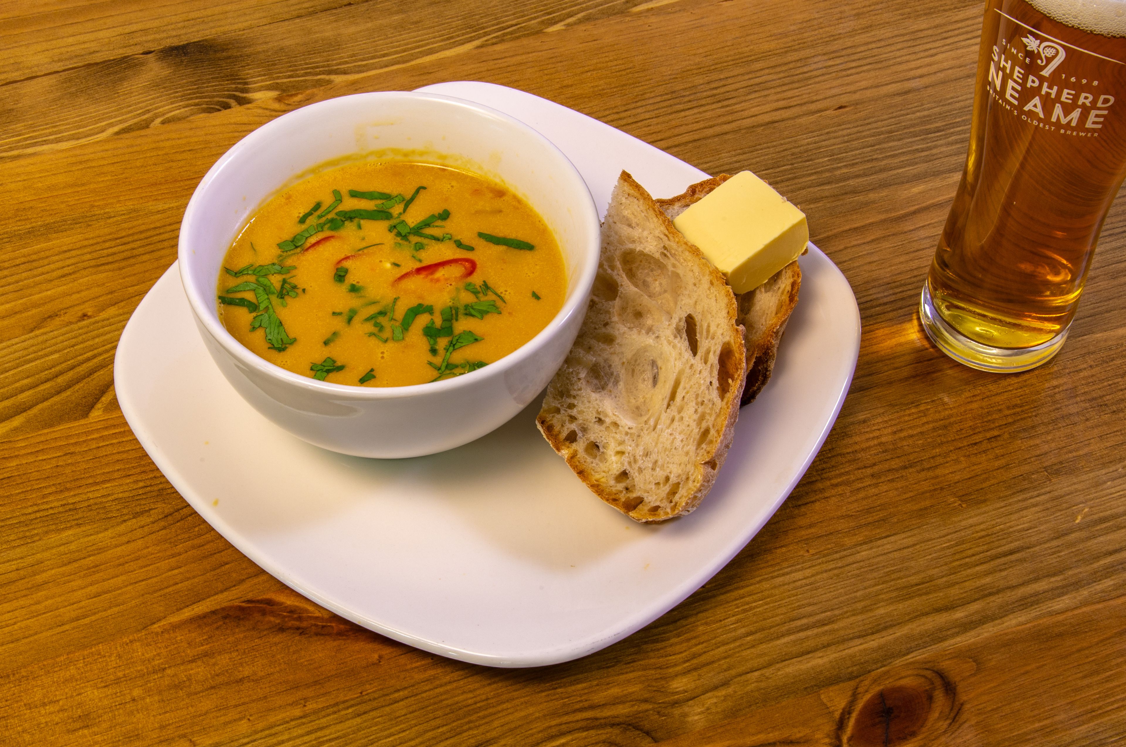 Un bol de soupe, une tranche de pain et un verre de bière sur une table en bois.
