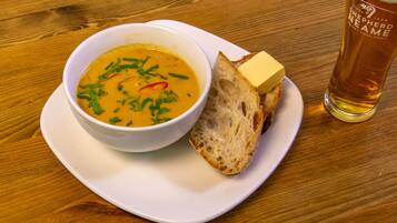 Un bol de soupe, une tranche de pain et un verre de bière sur une table en bois.