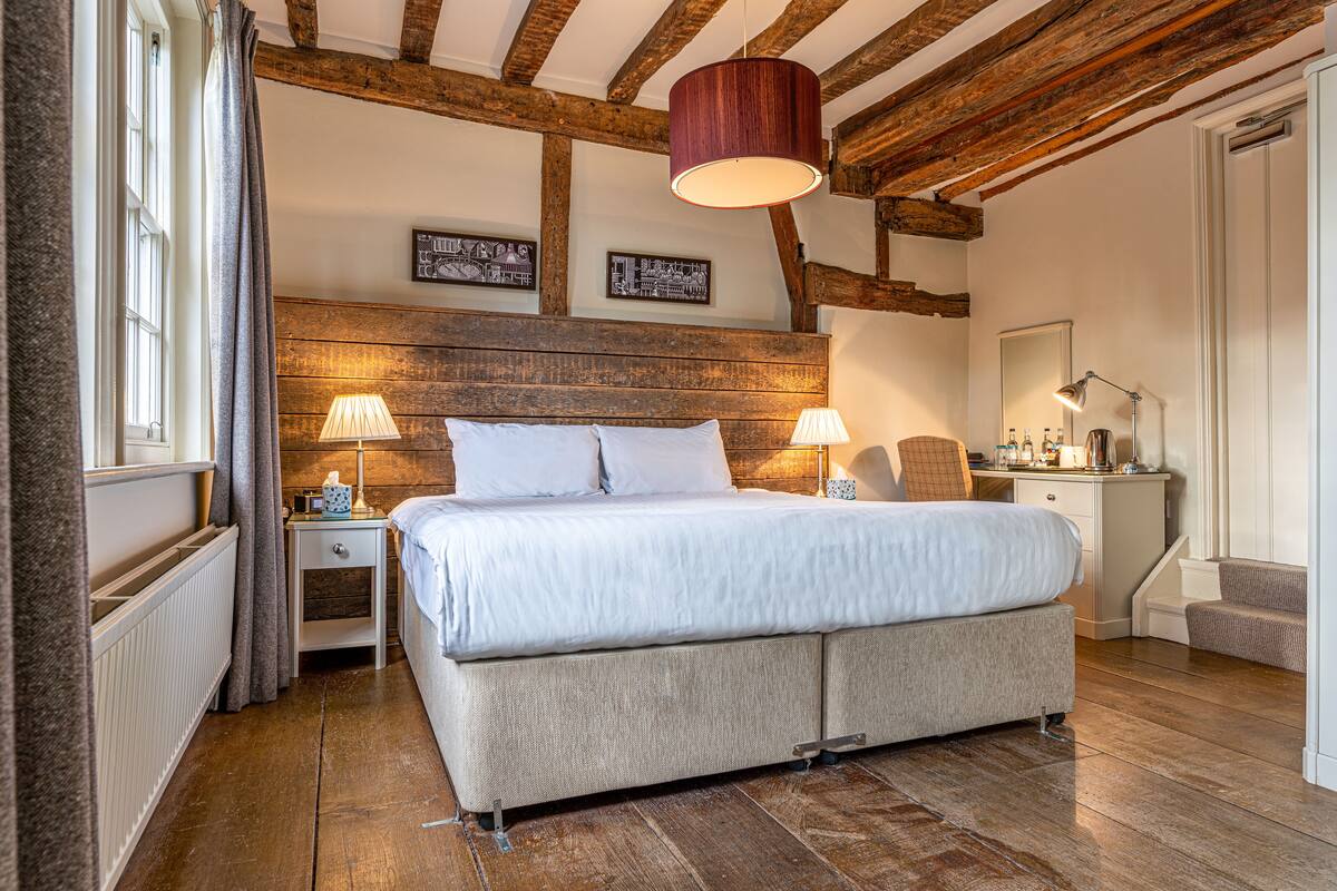 A bedroom with a wooden ceiling, a large bed, two bedside tables with lamps, and a small desk with a mirror.