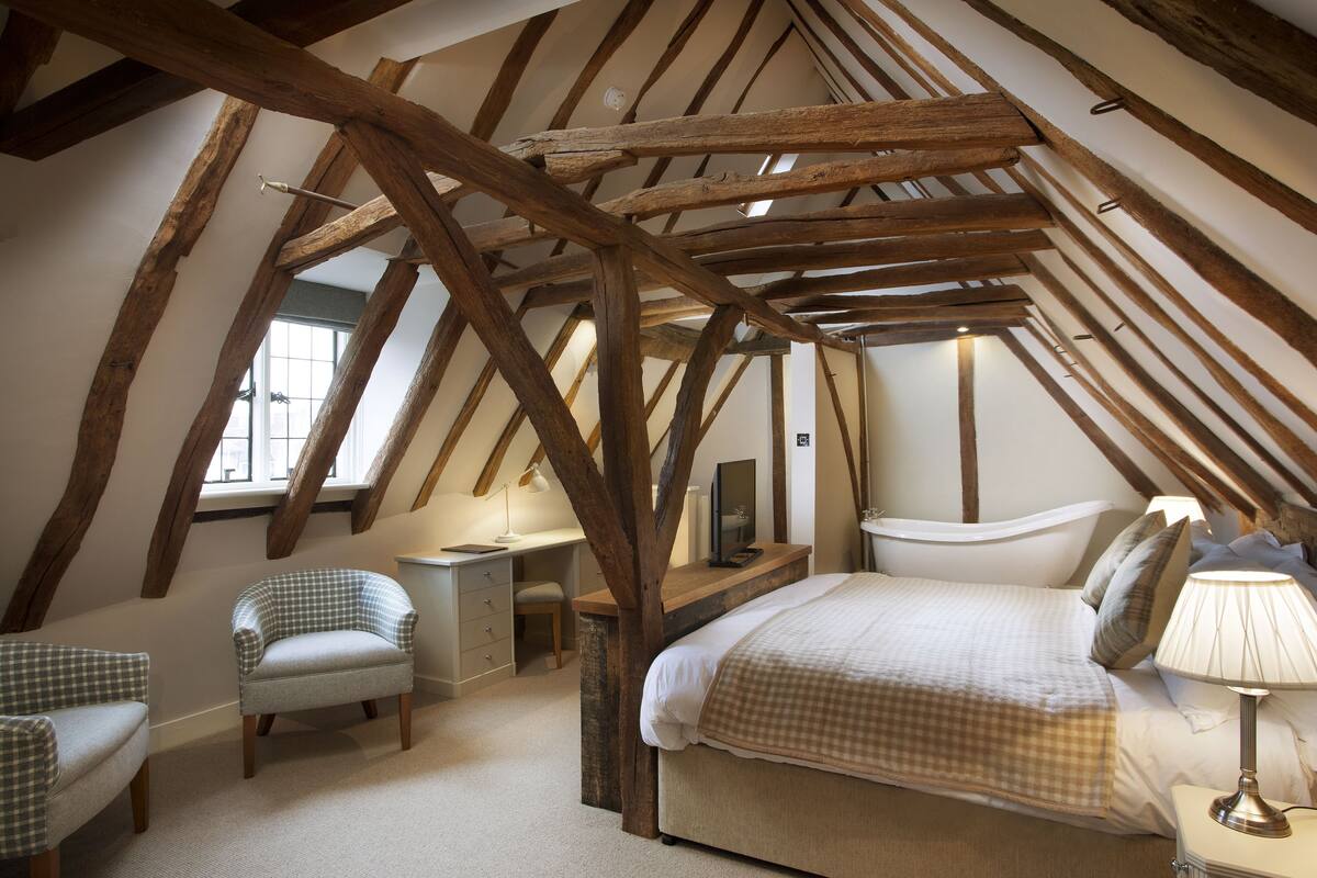 A bedroom with exposed wooden beams, a bed, a desk, and two chairs.