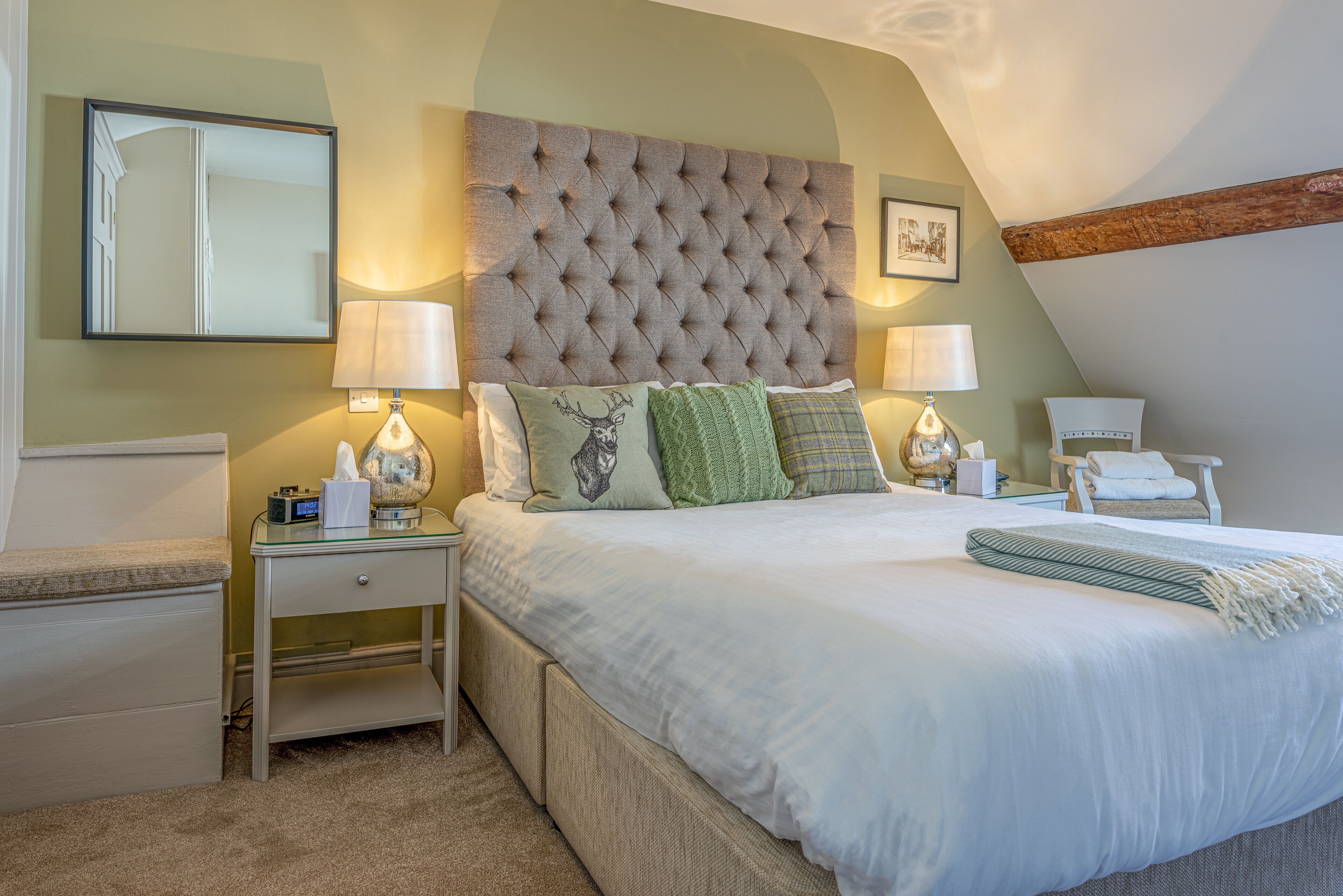 Une chambre à coucher avec une tête de lit capitonnée, deux tables de chevet avec des lampes, un lit avec une literie blanche et un fauteuil.