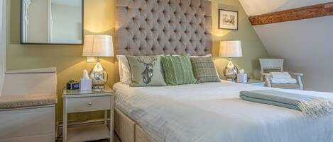 Une chambre à coucher avec une tête de lit capitonnée, deux tables de chevet avec des lampes, un lit avec une literie blanche et un fauteuil.