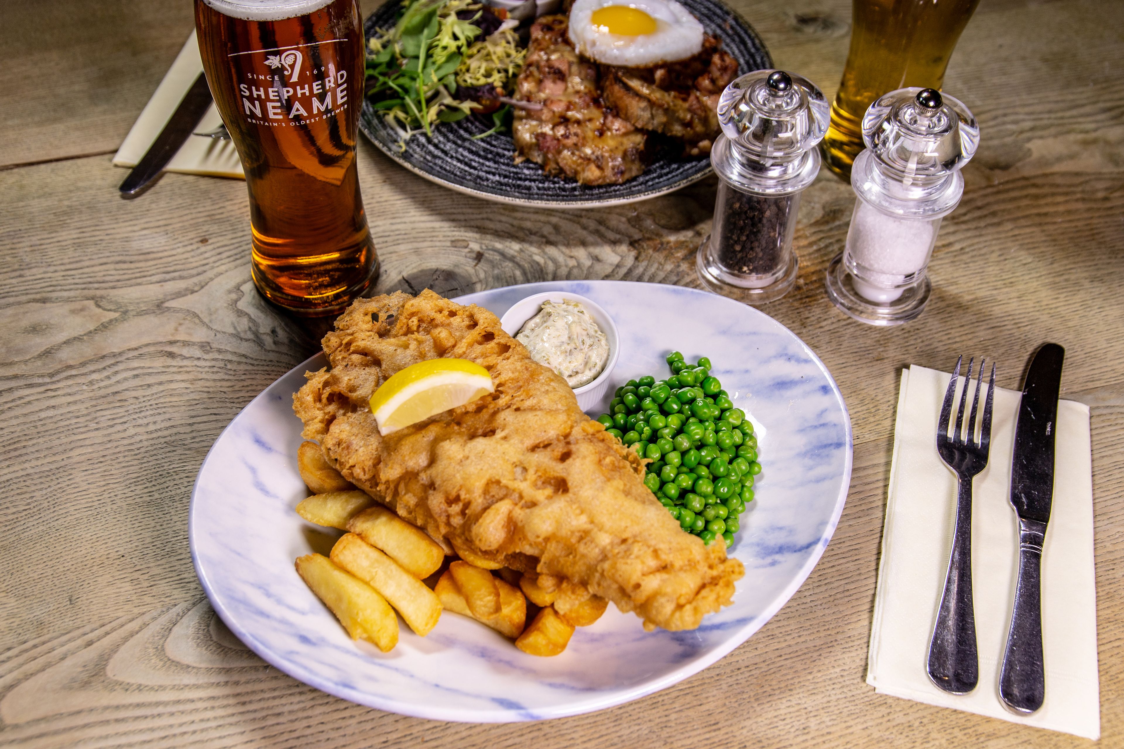 A plate of fish and chips with peas and a lemon wedge, a glass of beer, and a side salad.