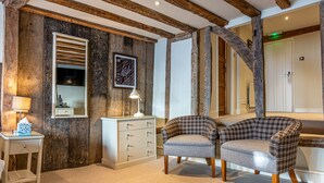 A room with exposed wooden beams, a white dresser, two plaid armchairs, and a mirror. - The Sun Inn (Faversham)