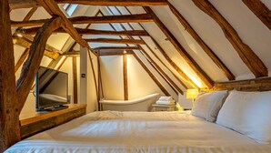 A bedroom with a large bed, a television, a bathtub, and wooden beams on the ceiling. - The Sun Inn (Faversham)