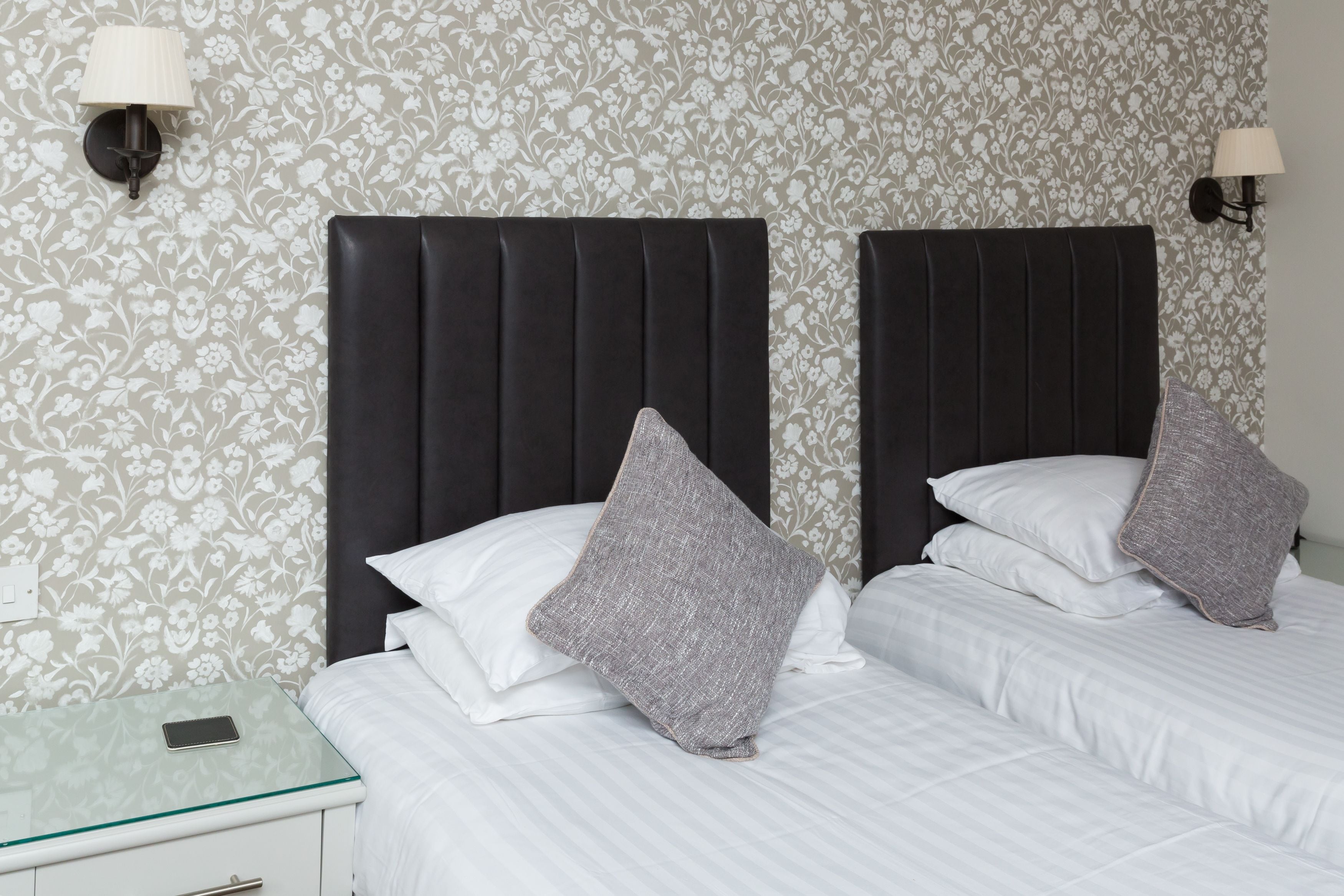 Een hotelkamer met twee bedden, elk voorzien van een donker hoofdbord en witte beddengoed. Aan weerszijden van de bedden hangen twee wandlampen.
