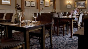 A restaurant with wooden tables and chairs, framed pictures on the walls, and a patterned carpet. - Dog & Bear Hotel (Maidstone)