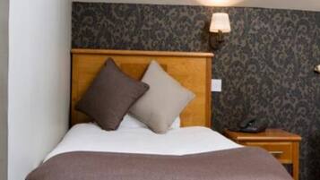 A bed with a wooden headboard, two pillows, a brown bedspread, and a nightstand with a lamp.