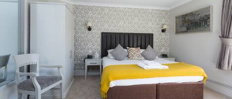 A bedroom with a bed, a nightstand, a chair, and a wall with a patterned wallpaper.
