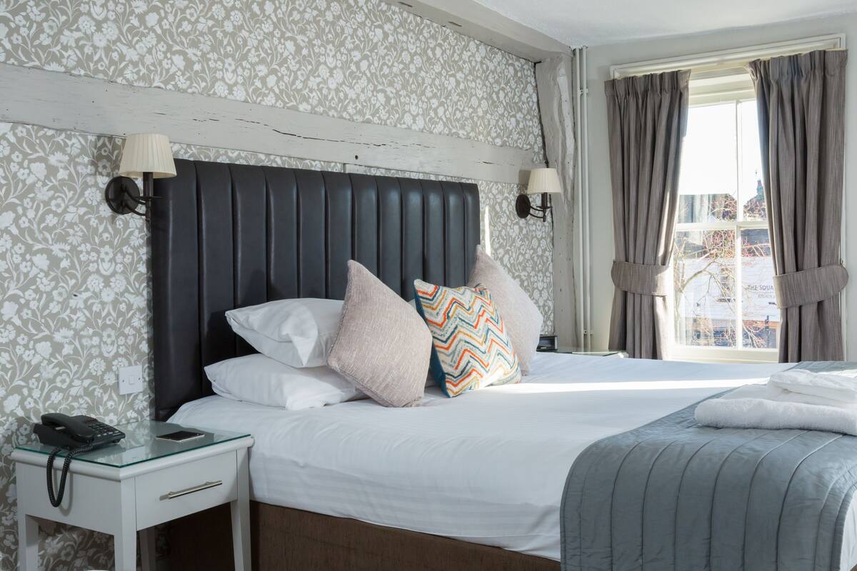 A hotel room with a bed, a nightstand with a phone, and a window with curtains.