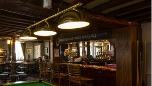 A billiards room with a pool table, wooden chairs, and a bar area with a sign indicating board and bar games are available. - Dog & Bear Hotel (Maidstone)