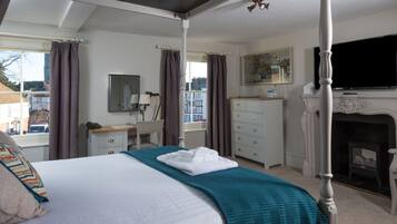 A four-poster bed with a teal throw blanket, a white dresser, a mirror, a television, and a fireplace.