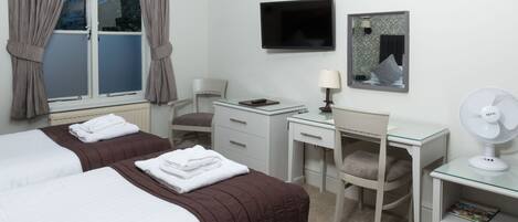 A hotel room with two beds, a desk, a chair, a TV, a mirror, and a fan.