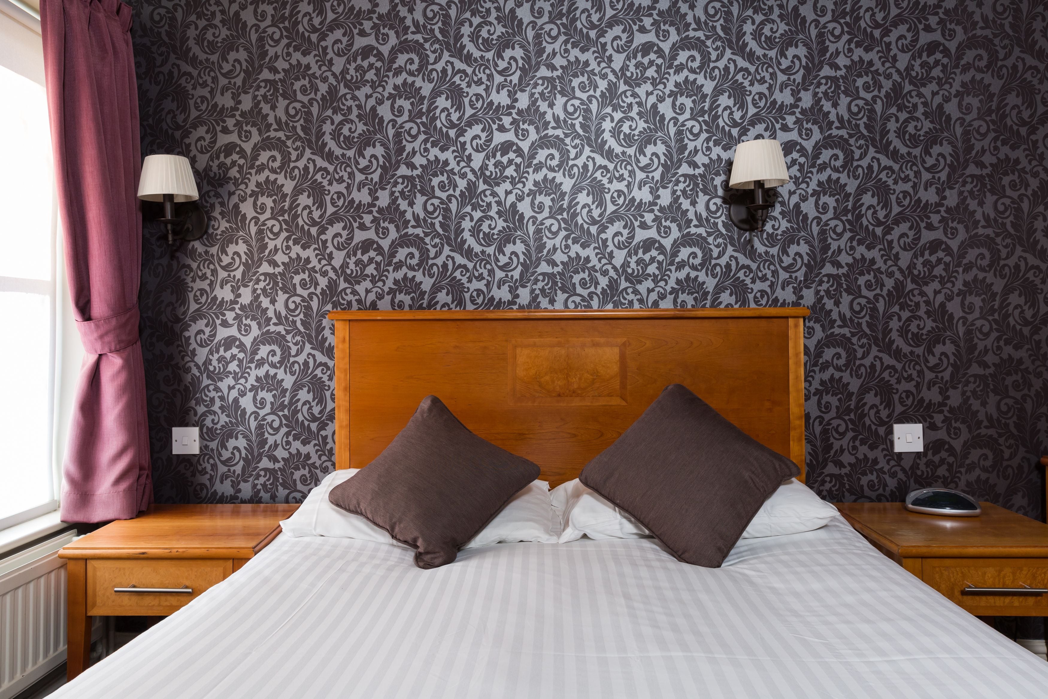 Een netjes opgemaakt bed met twee kussens, een houten hoofdbord en een nachtkastje met een lamp.