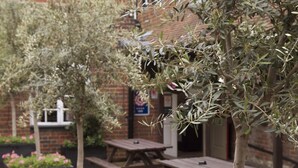 An outdoor patio area with wooden picnic tables and planters with flowers. - Dog & Bear Hotel (Maidstone)