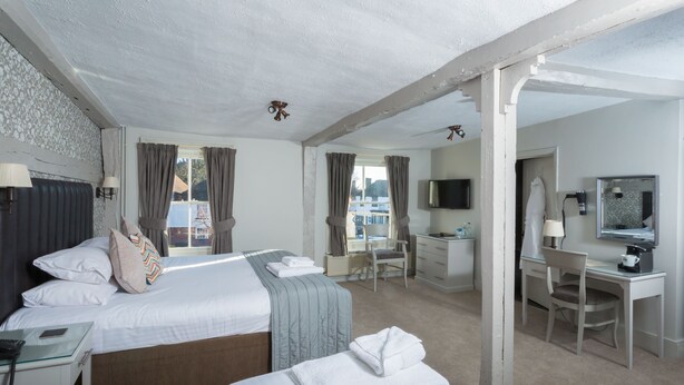 A hotel room with a large bed, a desk, a chair, a TV, and a bathroom visible through the window. - Dog & Bear Hotel (Maidstone)