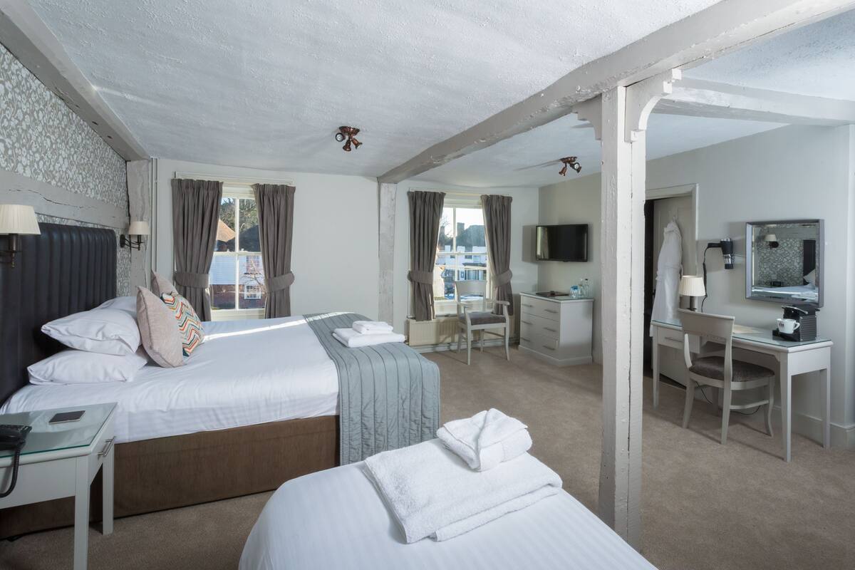 A hotel room with a large bed, a desk, a chair, a TV, and a bathroom visible through the window.