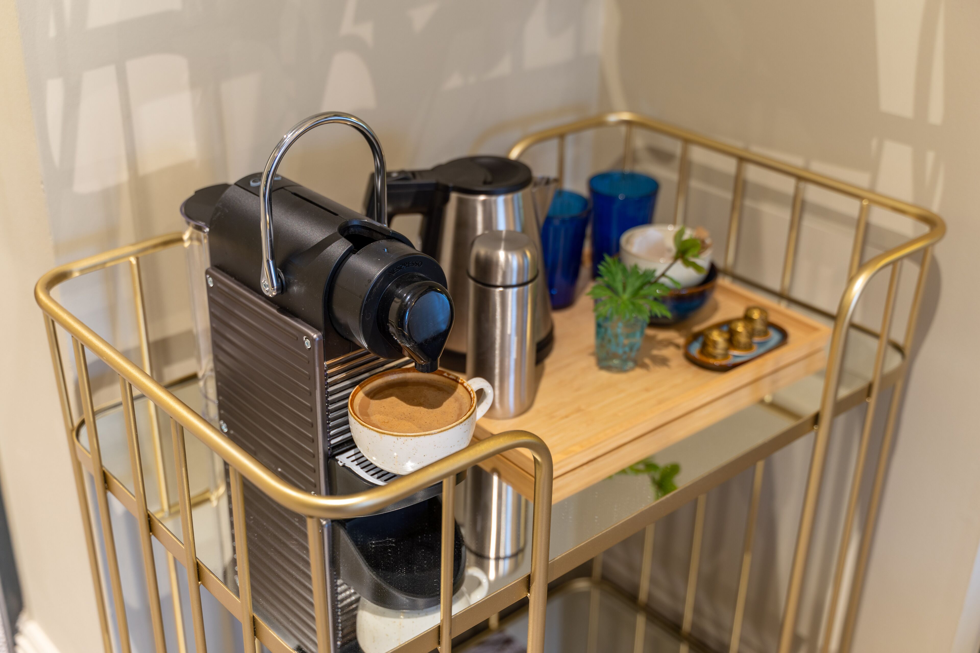 Una máquina de café sobre un carrito con una taza de café, una termo y una pequeña planta.